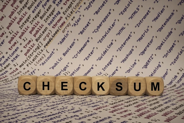 Wooden blocks spelling 'CHECKSUM' in front of a background filled with programming code and technical terms.