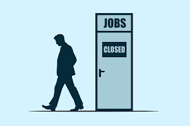 Silhouette of a man walking away from a door labeled “Jobs Closed,” representing unemployment or job shortage.