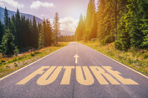 A road stretches into the distance, lined with tall evergreen trees on either side. The word 'FUTURE' is painted in large yellow letters on the asphalt, with an arrow pointing forward. The sun casts a warm glow over the scene, creating a sense of hope and possibility.