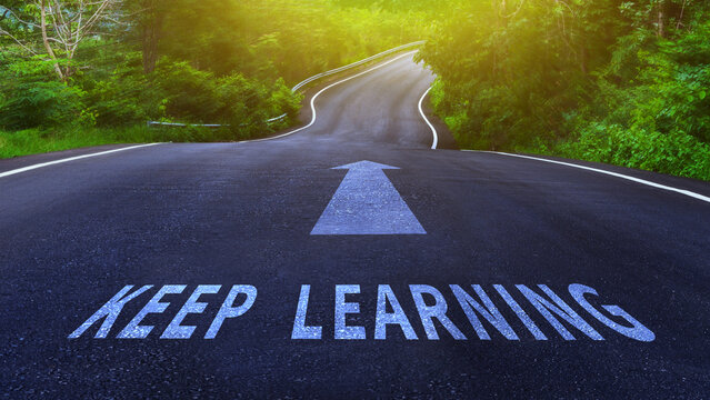 A winding road through a forest with an arrow and the words "Keep Learning" painted on the asphalt.
