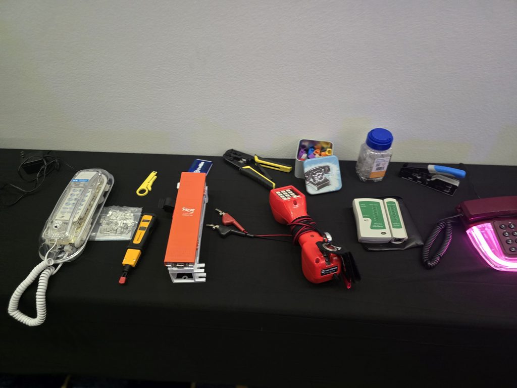 Telecommunications testing tools, lineman's handset, and vintage telephones on a black table.