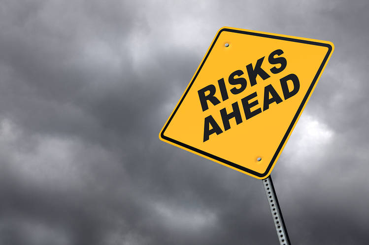 Yellow road sign reading “Risks Ahead” against a dark, cloudy stormy sky.