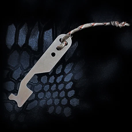 A small, flat metal latch bypass tool with a paracord lanyard, resting on a dark textured camouflage background